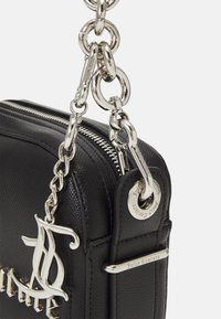 Svart läderhandväska med texturerad yta, silverfärgad hårdvara, kedjerem, framträdande logocharm och dragkedjestängning.
