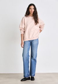 Sudadera de gran tamaño en rosa claro, con puños acanalados, combinada con unos vaqueros de pierna recta de lavado medio. Mocasines negros completan el conjunto.