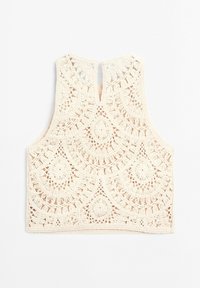 Haut court en crochet crème sans manches avec motifs circulaires et en éventail, encolure avec ouverture en forme de goutte d'eau, et bords festonnés, posé à plat sur fond blanc.