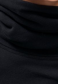 Černá pletená látka přeložená kolem výstřihu, zobrazující detailní šití a jemnou texturu.