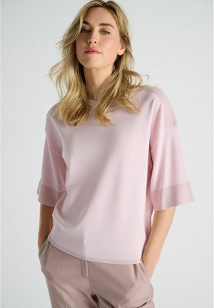 Lichtroze top met korte mouwen, afgewerkt met een gladde textuur en een subtiele metallic accent op de manchetten, gecombineerd met zachte, op maat gemaakte beige broek.
