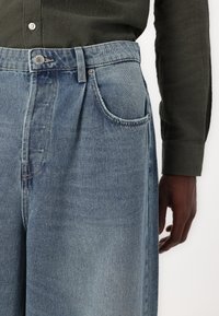 Ljusblå denimjeans med en avslappnad passform, med knappstängning, bälteshällor och sidofickor. Strukturerad tyg med synlig sömnad.