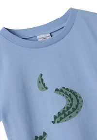 Vaaleansininen T-paita pyöreällä kauluksella, jossa on vihreä graafinen kuvio, joka näyttää abstrakteilta muodoilta, jotka muistuttavat eläinten suomuja tai aaltoja. Puuvillakangasta.