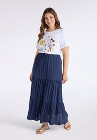 Maglietta bianca con grafiche colorate abbinata a una gonna maxi a balze blu navy, con vita regolabile e tessuto fluido.