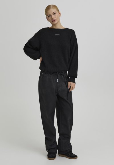 Fekete, túlméretezett kötött pulóver texturált anyaggal és vízszintes szegéllyel, laza fekete nadrággal, melynek derék részén zsinóros megkötő található.
