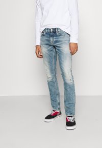 Ljusblå denimjeans med slitna detaljer, slim fit, femfickorsdesign, kombinerat med flerfärgade sneakers med svarta, röda och vita accenter.