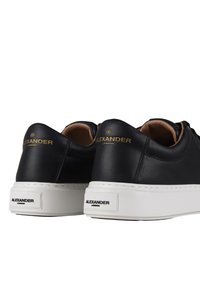 Sneakers in pelle nera con suola in gomma bianca, con un accento in oro sul tallone e una texture liscia. Design low-top.