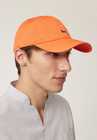 Oranžová baseballová čiapka z látky, s prešitými detailmi a malým čiernym logom siluety zvieraťa na prednej strane.