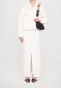 Bílá džínová bunda s velkými knoflíky nošená přes bílou maxi sukni s předním rozparkem. Černá kabelka s pletenými detaily a popruhem. Černé sandály.