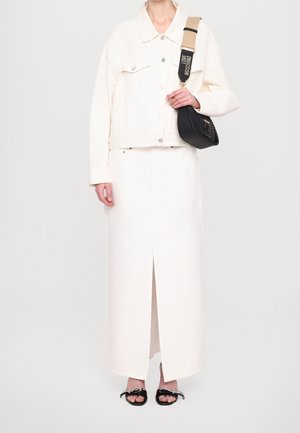 Hvid denimjakke med store knapper, båret over en hvid maxiskirt med slids foran. Sort håndtaske med flettet detalje og rem. Sorte sandaler.