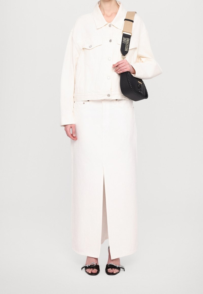 Bílá džínová bunda s velkými knoflíky nošená přes bílou maxi sukni s předním rozparkem. Černá kabelka s pletenými detaily a popruhem. Černé sandály.