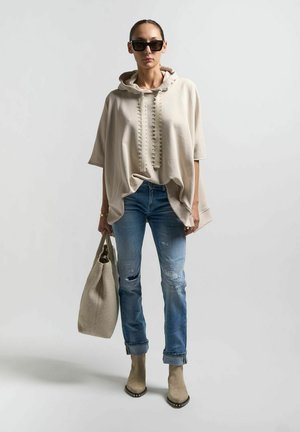 Felpa oversized beige con collo testurizzato, jeans blu strappati, stivali beige alla caviglia e borsa a tracolla intrecciata grigia chiara.