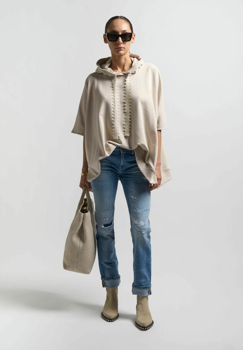 Felpa oversized beige con collo testurizzato, jeans blu strappati, stivali beige alla caviglia e borsa a tracolla intrecciata grigia chiara.