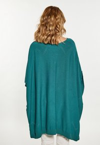 Poncho tricotat teal cu o croială lejeră, având un model în zigzag creat prin detalii de lucru deschis pe spate și un tiv striat.
