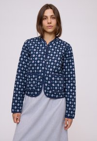 Giacca trapuntata blu navale con motivo a rombi, chiusura con zip, scollo rotondo e due tasche anteriori con bordo a contrasto. Tessuto leggero.