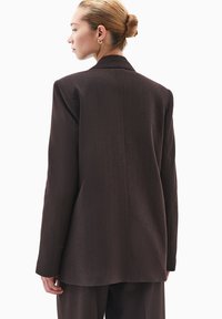 Blazer marrón a medida con cuello muesca, mangas largas y corte recto, que presenta una textura suave y un diseño minimalista.