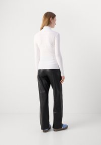Pull en col roulé blanc ajusté, texture côtelée, associé à un pantalon en cuir noir et des baskets bleues avec des semelles brunes. Design minimaliste.