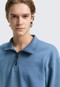 Hellblaues Zip-up Sweatshirt mit Kragen, aus weichem Stoff gefertigt. Verfügt über einen Frontreißverschluss und eine entspannte Passform, die eine glatte Textur zeigt.
