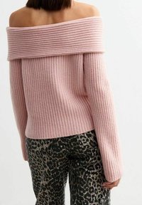 Maglione rosa chiaro a coste con spalle scoperte e maniche lunghe; abbinato a pantaloni con stampa leopardata nera e grigia con tasche posteriori.