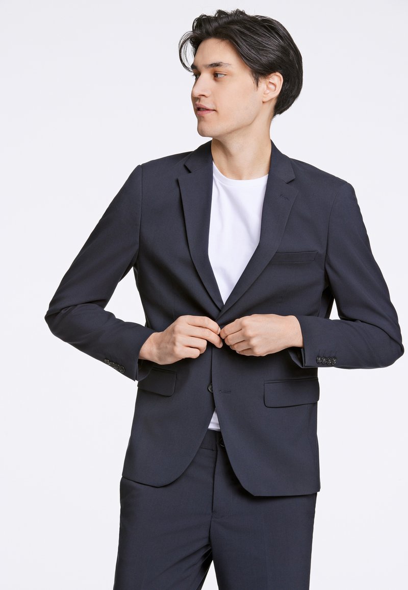 Blazer blu navy con rever a scialle, chiusura con un bottone e due tasche frontali. Design sartoriale con tessuto liscio e leggero lucido.