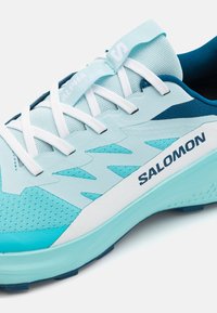 Lyseblå løpesko med mesh- og syntetiske materialer, et strømlinjeformet design, hvite snørebånd og "SALOMON"-logo på siden.