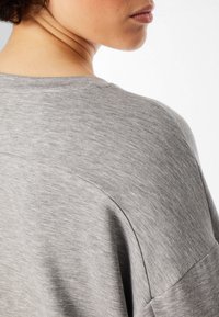 T-shirt in cotone grigio, con una vestibilità rilassata, scollo rotondo e texture morbida, caratterizzato da dettagli di cucitura visibili sulla spalla.
