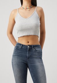 Top cropped gris con textura acanalada y dobladillo sin acabar, combinado con unos jeans ajustados azules que presentan un diseño clásico de cinco bolsillos.