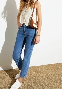 Ljusfärgad, knäppt väst med vertikala ränder, ihop med blå denimjeans och vita sneakers. Liten brun axelväska.