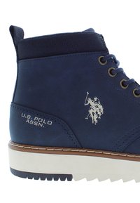 Mörkblå U.S. Polo Assn. hög-top sneakers med vit sula, metallöglor, vadderad vristkrage och polospelarlogotyp på sidan.