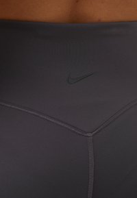 Leggings de sport gris en tissu lisse et extensible, avec un logo Nike discret et des coutures détaillées.