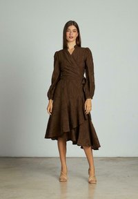 Rochie maro, cu mâneci bufante lungi, din material texturat și tiv în straturi. Stilizată cu sandale cu toc bej.