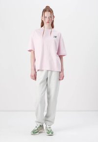 Light pink oversized t-shirt with a small multicolored logo on the chest, paired with light gray sweatpants and green shoes. Simple design.