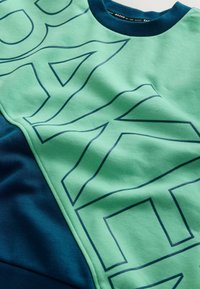 Zielona i granatowa bluza z dużym, ciemnoniebieskim napisem. Projekt ma gładką teksturę z okrągłym dekoltem oraz kolorowymi sekcjami.