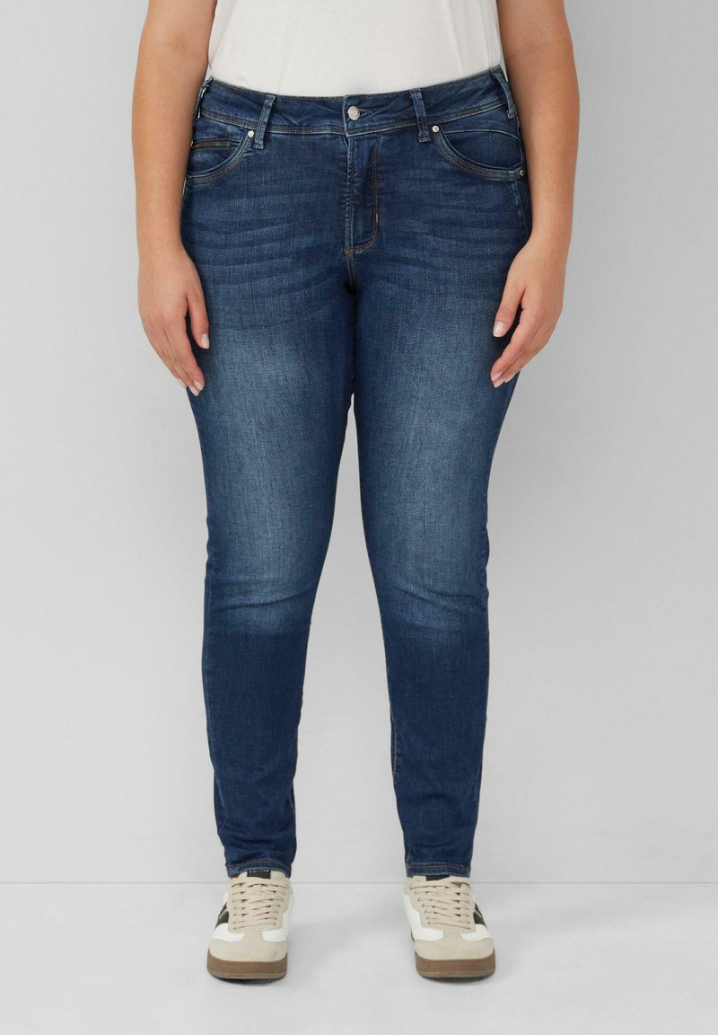 Donkerblauwe denim jeans met een slim fit, voorzien van voorzakken, een knoopsluiting en subtiele vervaging voor textuur. Draag ze met lichte sneakers.