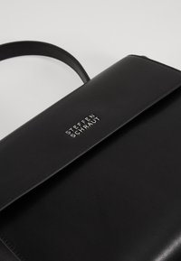 Sac à main en cuir noir au design élégant, avec une fermeture à rabat et un logo embossé en argent. Texture lisse avec une seule bandoulière.