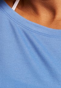 Blå bomullstyg med en slät yta och svag lyster. Har en rundad halsringning med fina stygn och tunna, vita band synliga.