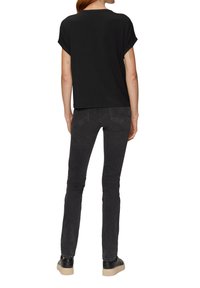 Zwart top met korte mouwen en een losse fit, gecombineerd met donkergrijze skinny jeans. De outfit wordt compleet gemaakt met zwarte schoenen met een licht beige zool.