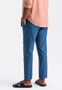 Pantalon bleu en tissu léger, avec une coupe droite et des poignets roulés. Assorti à des sandales noires pour un look décontracté.