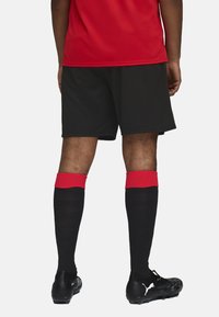 Pantalones cortos negros con un acento rojo en la cintura, combinados con calcetas negras hasta la rodilla con puños rojos y botas negras.