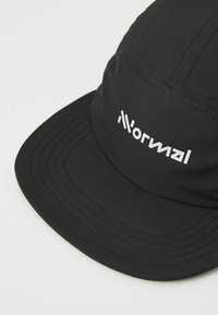Black cap with a flat brim, made of textured fabric. Features white logo on the front and distinct stitching patterns.