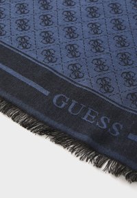 Écharpe bleu marine avec un motif de logo noir, présentant des bords effilochés et une texture de tissu lisse. "GUESS" est affiché en bleu foncé.