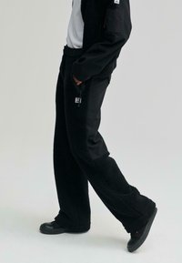 Fleece textúrájú fekete nadrág, sima szövetpanelek, elülső cipzáros zsebek és logófolt a combján.