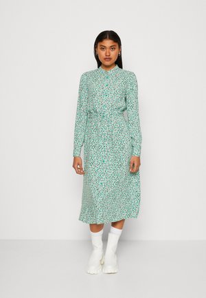 Pika-sleeve, nööbidest kleit helesiniselt lillemustriga; omab vöörihmaga taljet ja voolavat seelikut, millele on lisatud valged pahkluu saapad.
