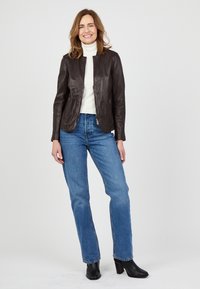 Braune Lederjacke mit taillierter Passform, Reißverschlusstaschen und Stehkragen, kombiniert mit blauen, geraden Jeans und schwarzen, hohen Stiefeln.