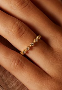 Gouden ring met vijf heldere stenen, met ingewikkelde details en een gestructureerde band. Draagt op een hand met een warme huidtint.