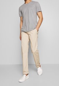 Gray short-sleeve t-shirt, beige chinos, and white slip-on shoes. Chinos feature a relaxed fit and subtle texture. Simple and casual ensemble.