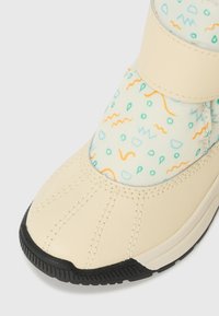Beige Sneaker mit einem gemusterten, hellblauen Obermaterial aus Stoff, das aquafarbene und orangefarbene geometrische Formen aufweist. Schwarze Gummisohle mit strukturiertem Grip.