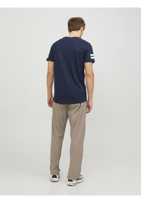 Camiseta azul marino con rayas blancas en las mangas, combinada con pantalones beige. La tela parece suave, con un corte relajado y un escote estándar.