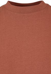 Gros plan d'un t-shirt col rond couleur rouille montrant la texture du tissu et les coutures autour de l'encolure.