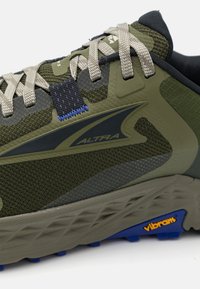 Zelená sportovní bota s texturovaným síťovaným svrškem, šedými a tmavými akcenty, šněrováním a modrým detailem na podrážce Vibram pro trakci.